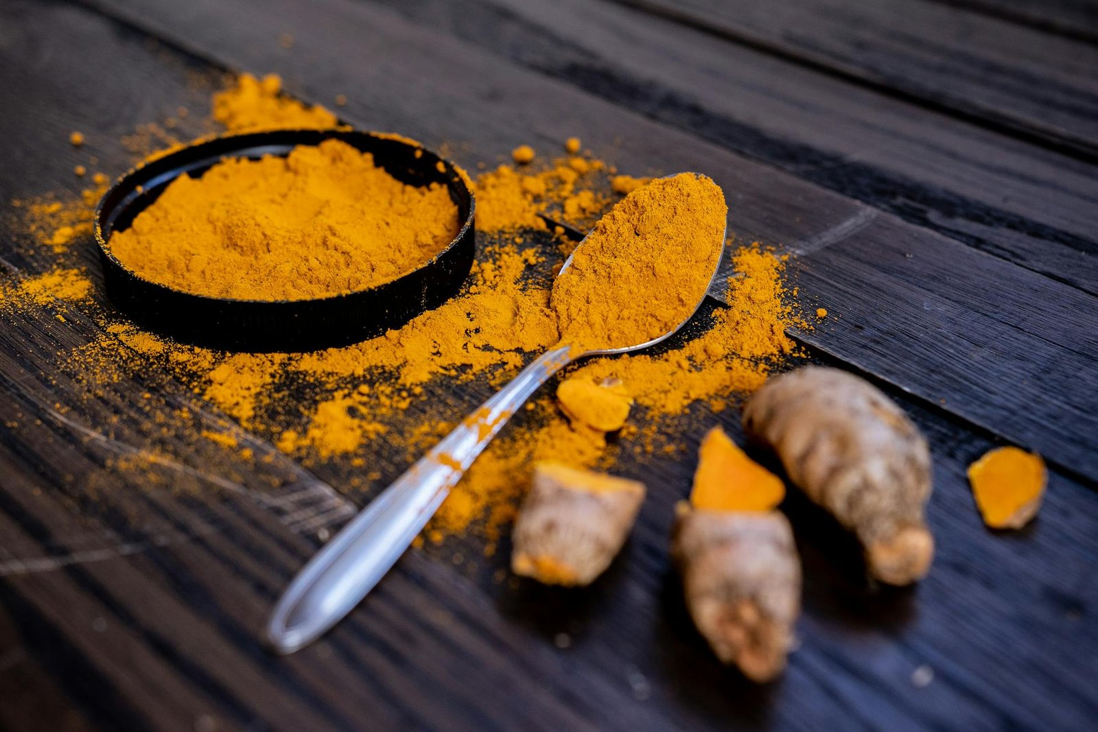 Anti-inflammatory spices including fresh turmeric root, ginger, cinnamon sticks, black pepper, garlic and cloves arranged on dark stone surface