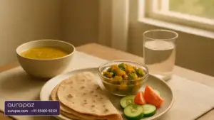 A plain home-cooked Indian lunch of rotis, dal, mixed vegetable sabzi, cucumber and tomato slices and a glass of water on a table by a window
